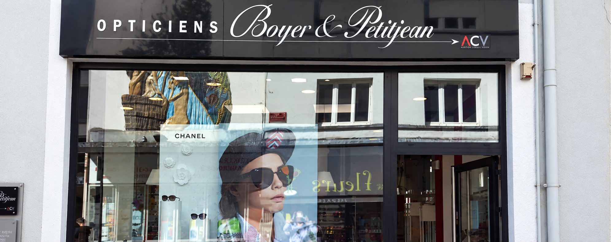 Façade sombre d'un magasin d'opticien dont la vitrine présente une affiche Chanel d'une femme portant des lunettes de soleil.