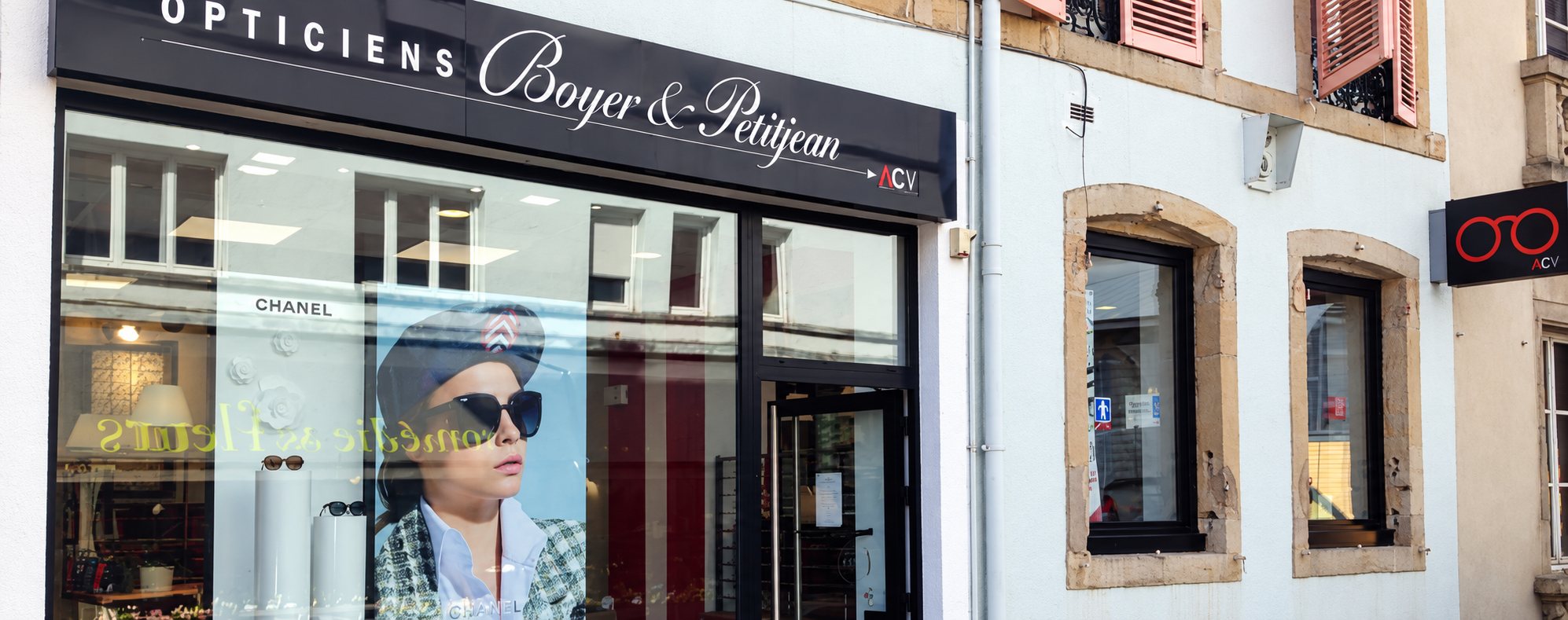 Devanture de l'opticien Boyer & Petitjean avec une grande vitrine ornée d'une affiche de femme portant des lunettes de soleil et une enseigne ACV sur la droite.