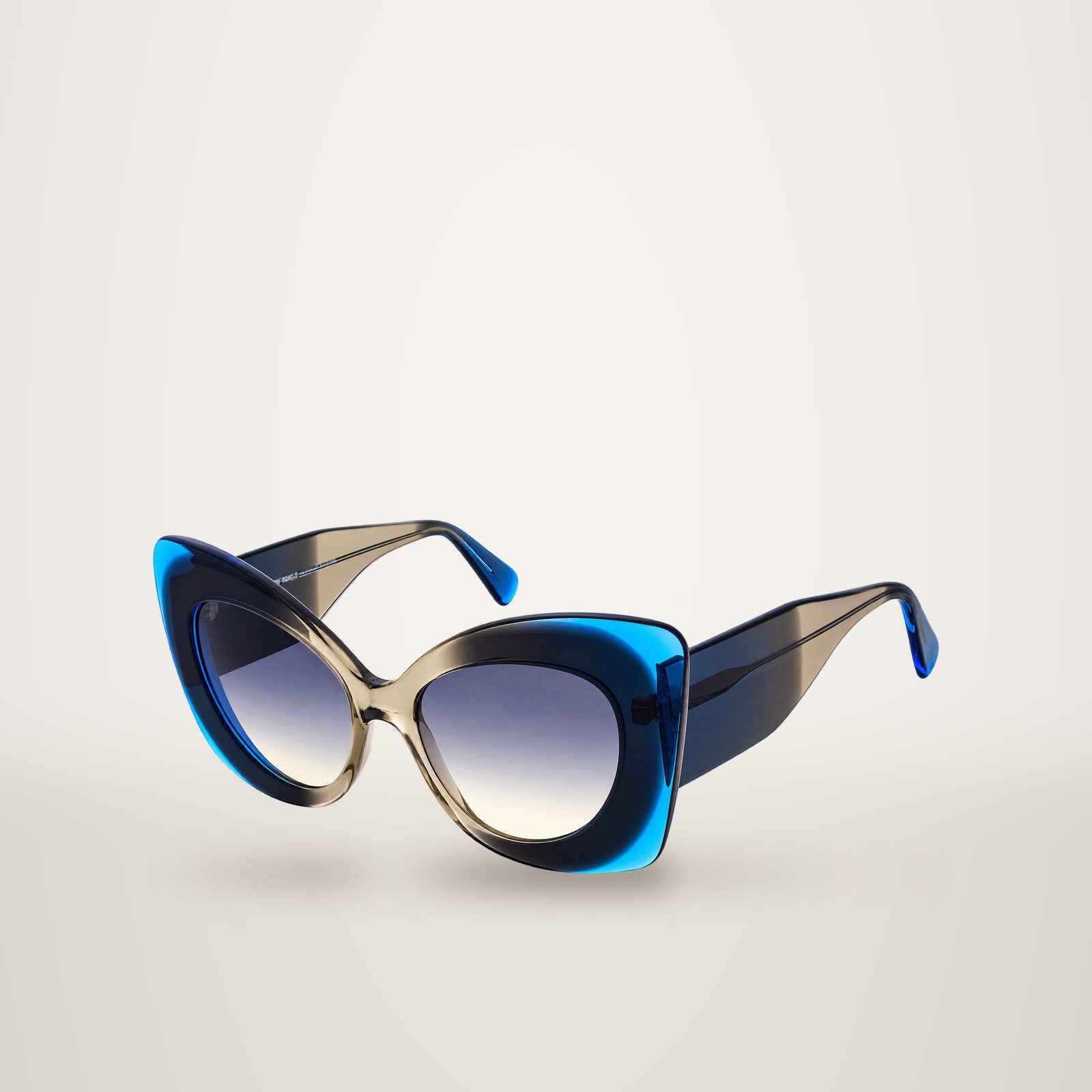 Paire de lunettes de soleil de forme papillon surdimensionnée, monture translucide bleue et grise, avec verres dégradés, présentée sur fond blanc.
