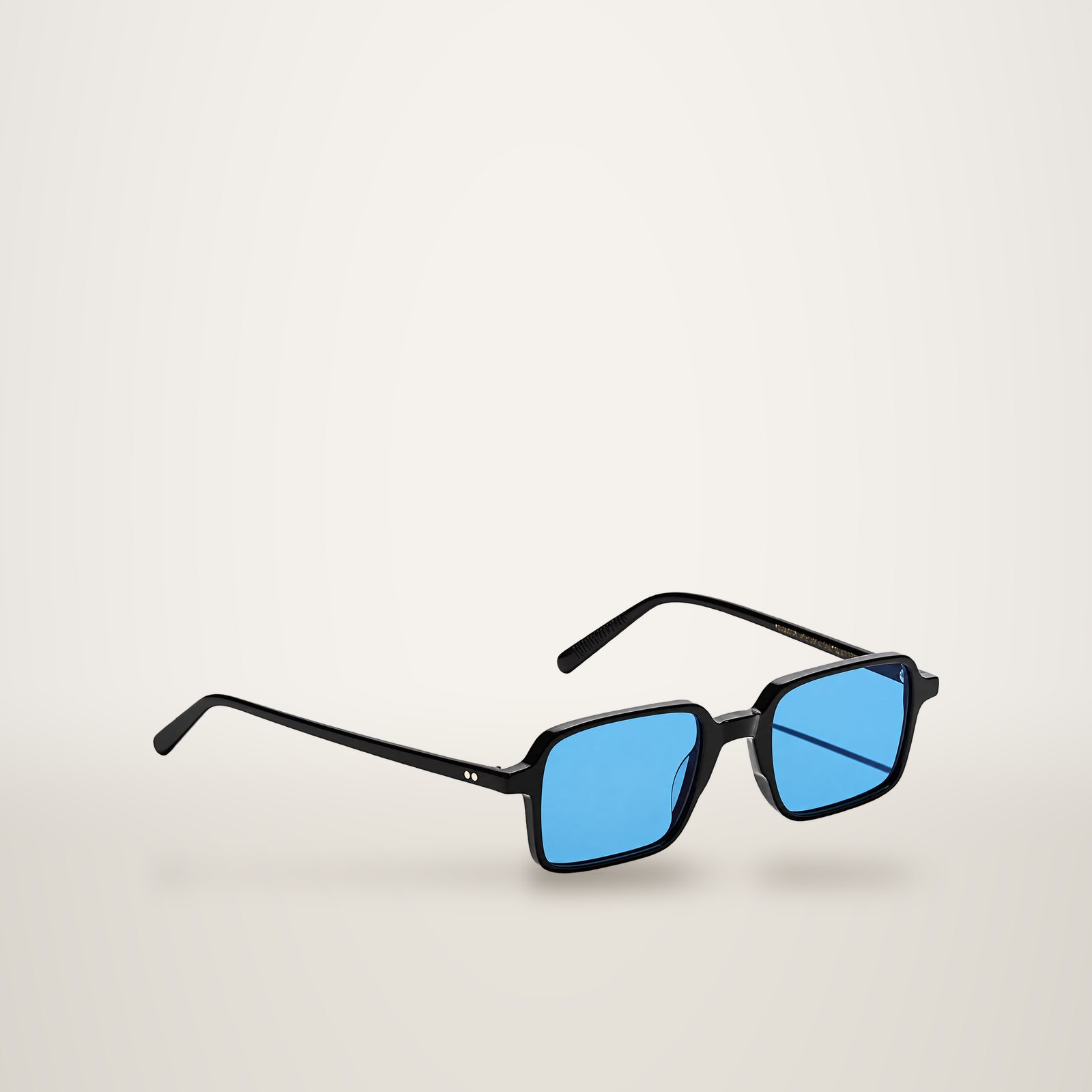 Paire de lunettes de soleil à monture rectangulaire noire et verres bleus, posée sur un fond clair uni avec une ombre portée.