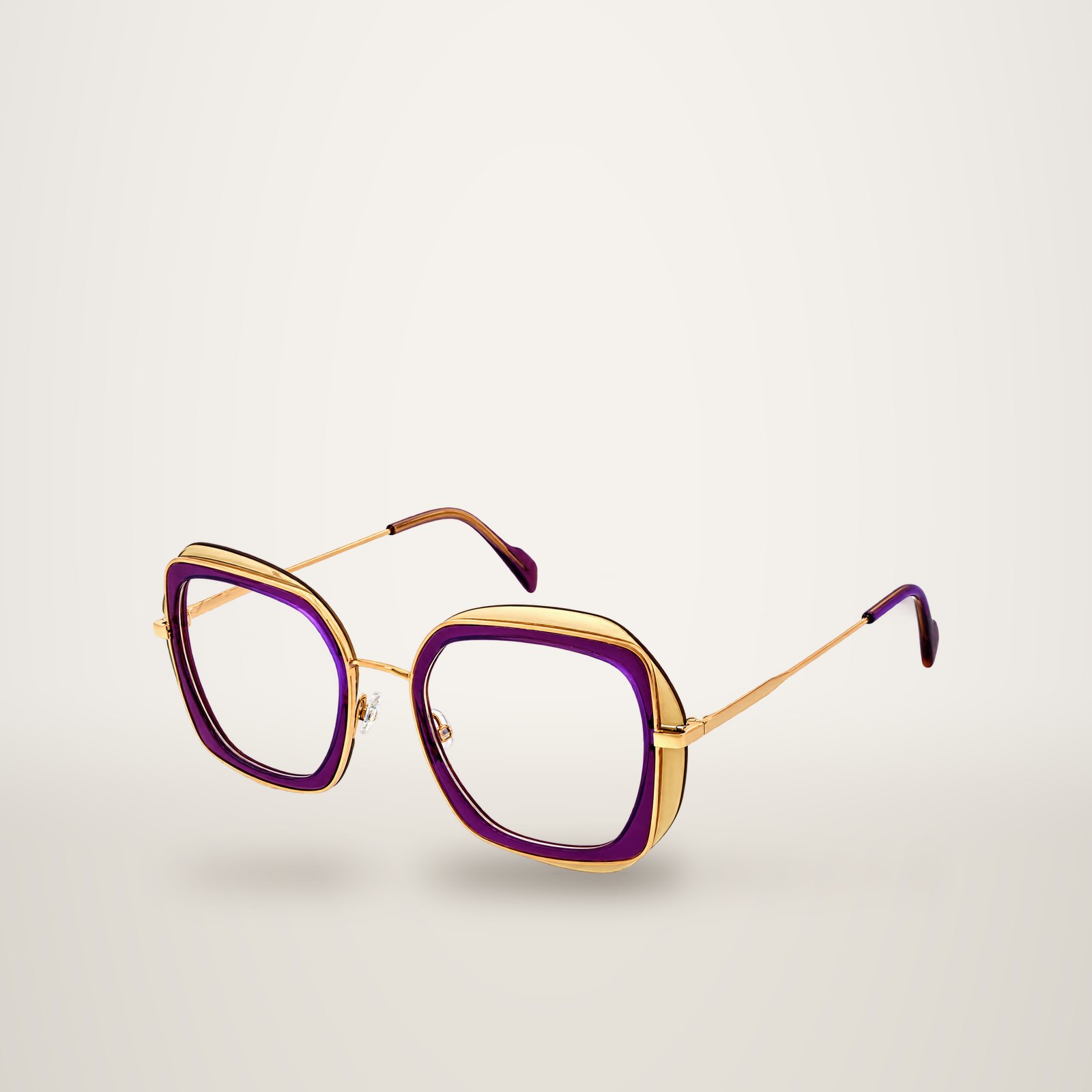 Monture de lunettes oversize aux formes carrées arrondies, en acétate violet translucide et métal doré, avec fines branches dorées, présentée sur fond blanc.