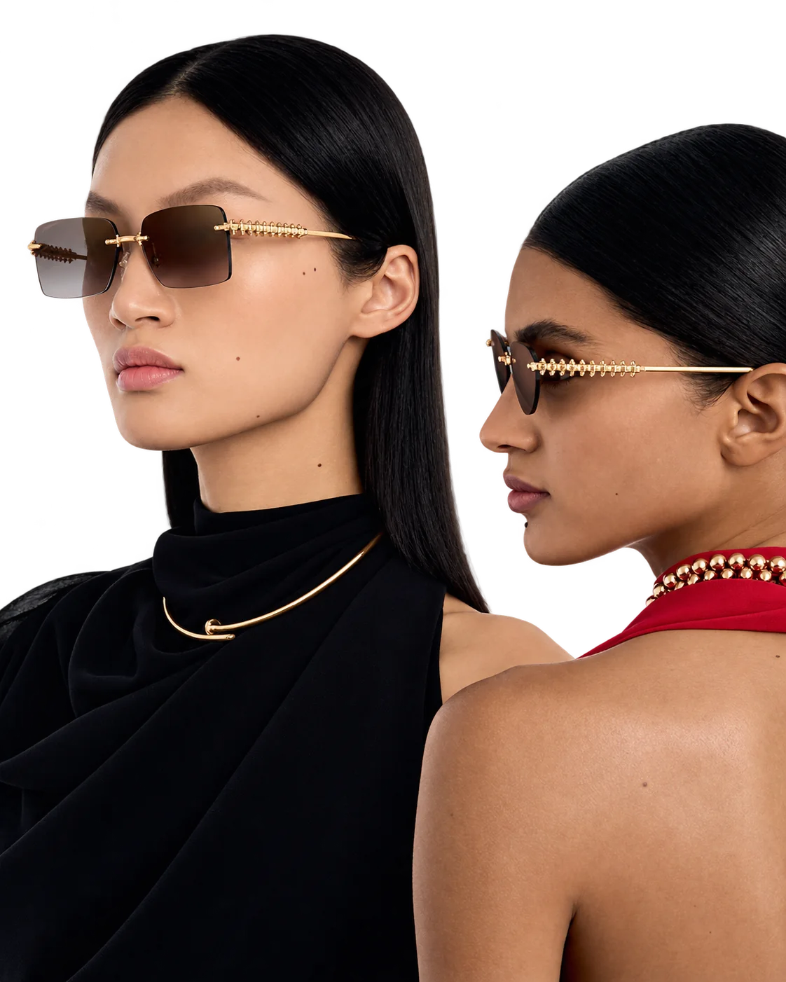 Deux femmes aux cheveux noirs lissés posent de profil avec des lunettes de soleil sans monture aux branches dorées, l'une portant un collier doré, l'autre un collier de perles dorées.