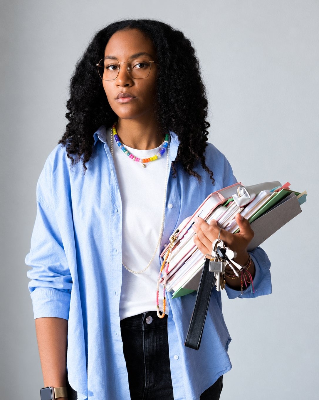 Portrait d’une jeune femme en chemise bleue, colliers et lunettes.